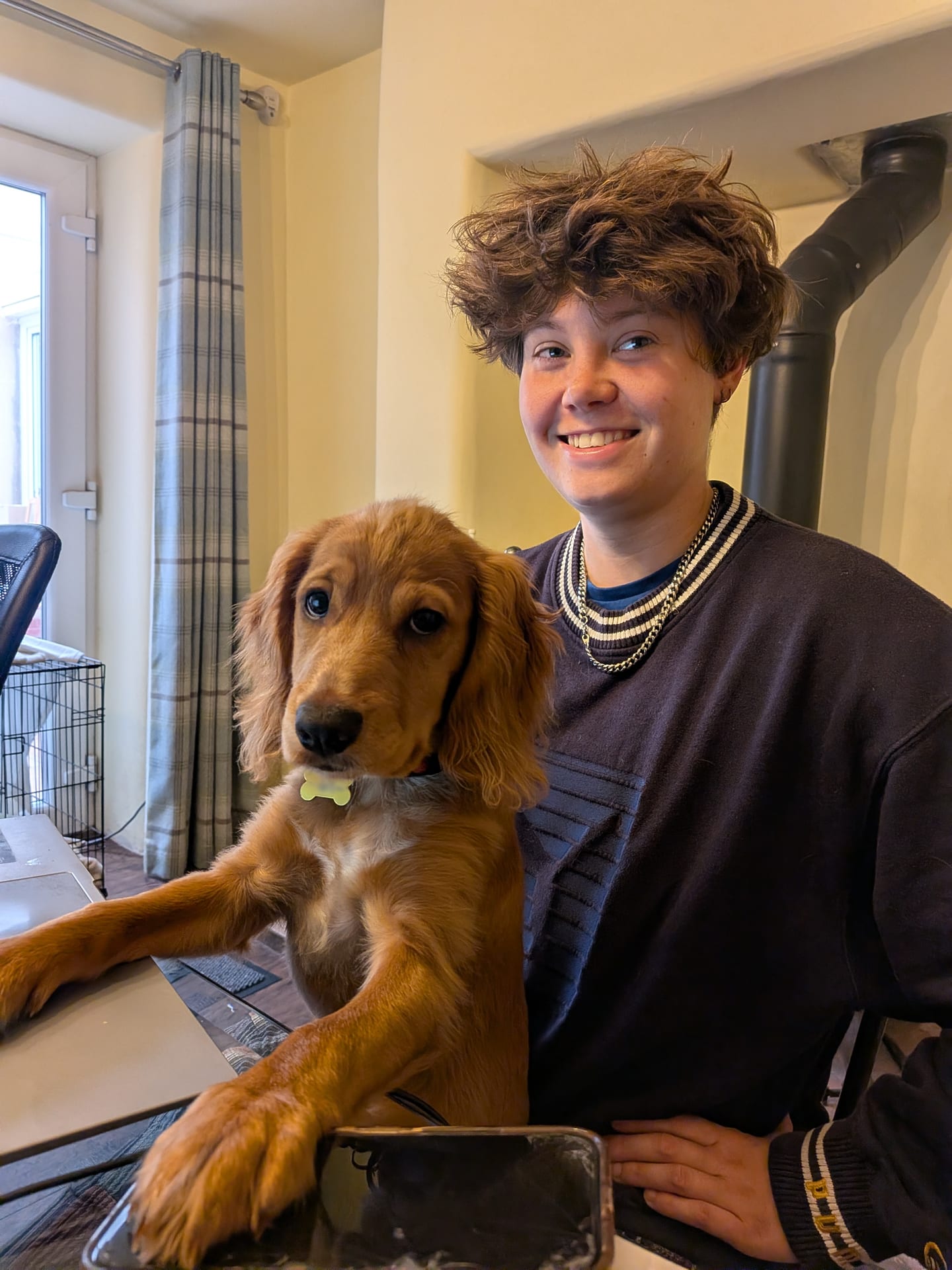Theo, smiling, sits at a desk beside Robin, a golden spaniel puppy with both front paws up on the desk next to a laptop.